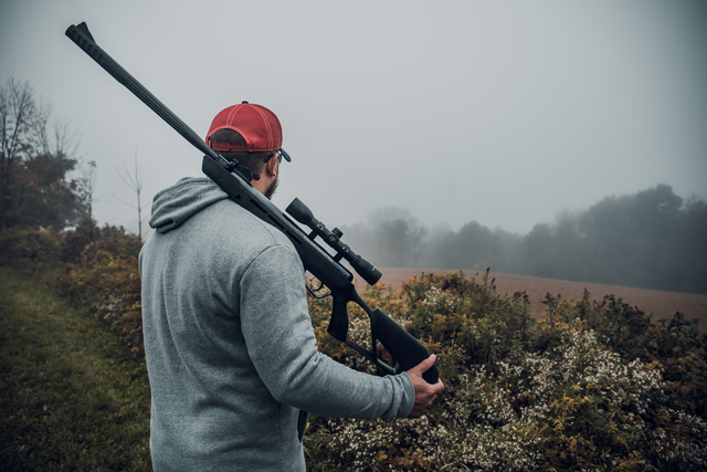 a man in a misty field holding an air rifle on his back