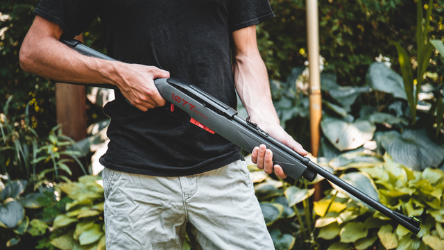 a man holding air gun in front of some plants
